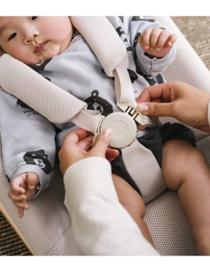 Manos abrochando el arnés de seguridad a un bebé en la hamaca Yoga de Stokke.