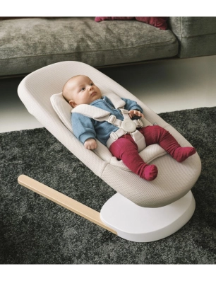 Bebé recostado y sujeto con arnés en la hamaca Yoga de Stokke sobre alfombra oscura.