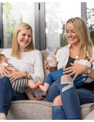 Dos mujeres dando el pecho a dos bebés con un Recolector Leche Generation 3 de Haakaa en la mano.