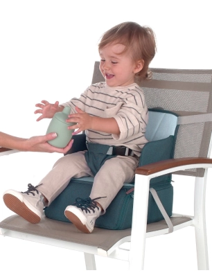 Niño sentado en la Trona de Viaje de Jané colocada sobre una silla, sujetado con arnés y recibiendo un vaso