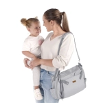 Madre con niña en brazos llevando la Trona de Viaje Avant de Jané U05 Dim Grey como bolso al hombro