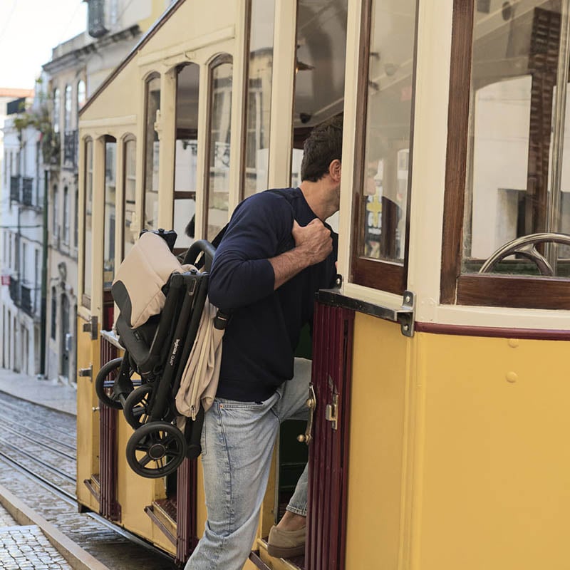 Silla de paseo Inglesina Quid 3 Beige plegada y siendo cargada por un padre. Silla de paseo Inglesina Quid 3 Beige plegada y siendo cargada por un padre.